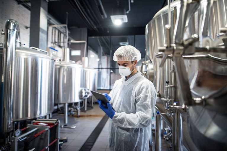 Cleanroom worker using a tablet to inspect a stainless steel tank during an asset maintenance check.