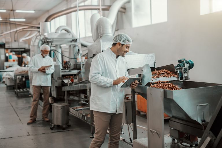 Food manufacturing workers using tablets on the production floor to monitor equipment and log data