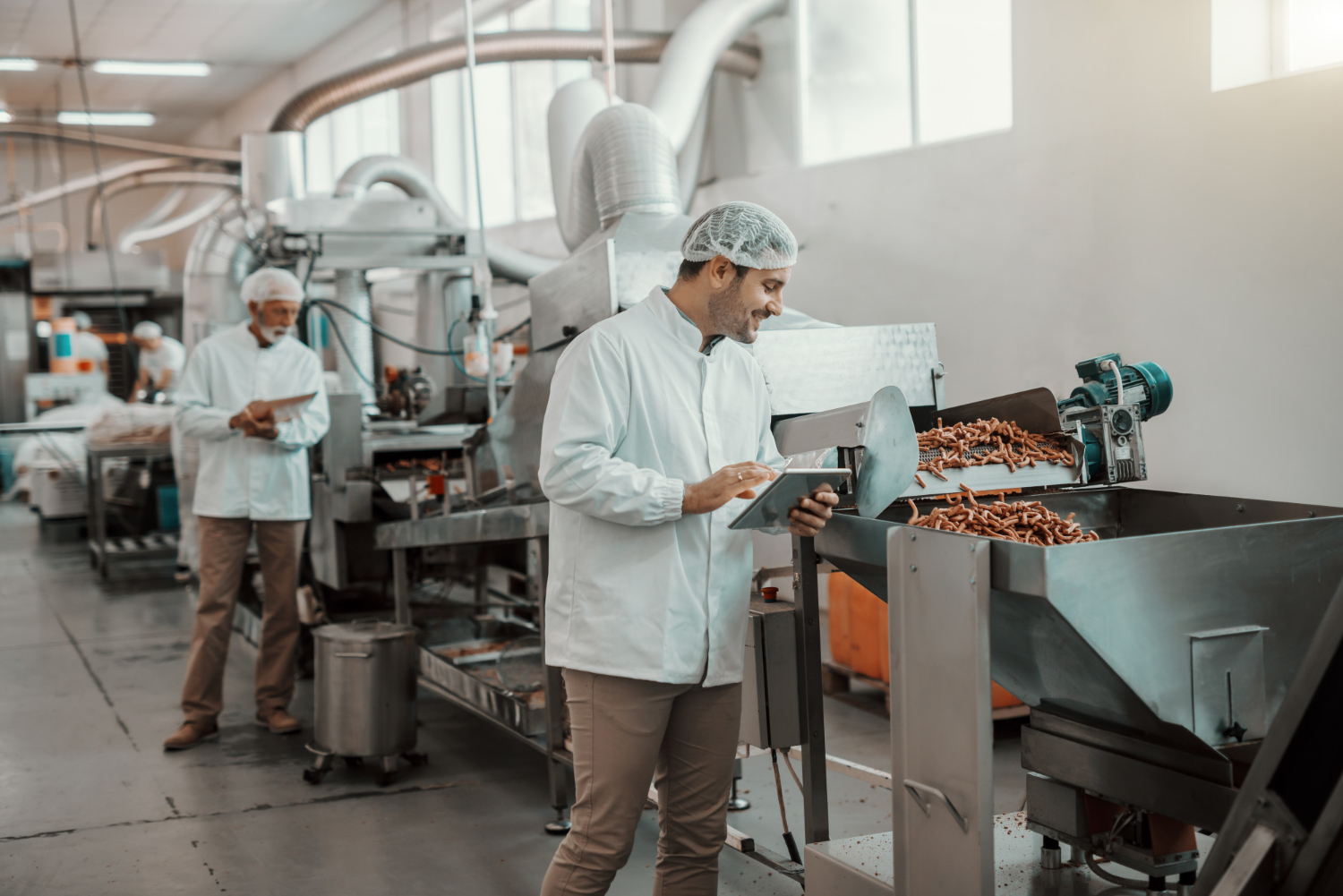 Food manufacturing workers using tablets on the production floor to monitor equipment and log data